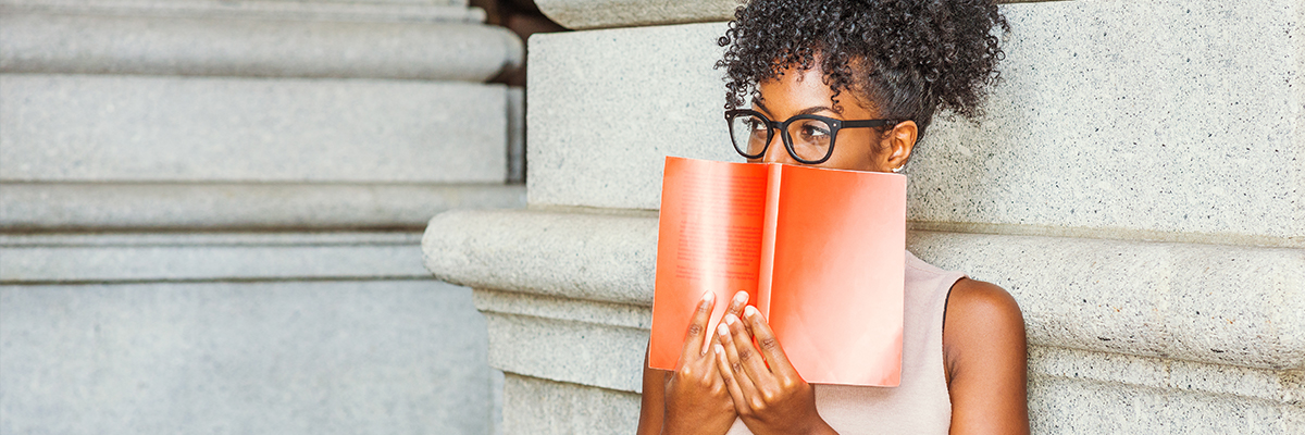 A woman wearing glasses holding a book in front of her face