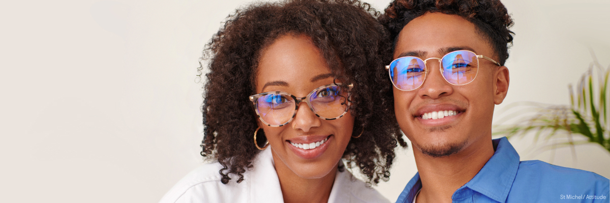 A man and woman smiling wearing blue light glasses